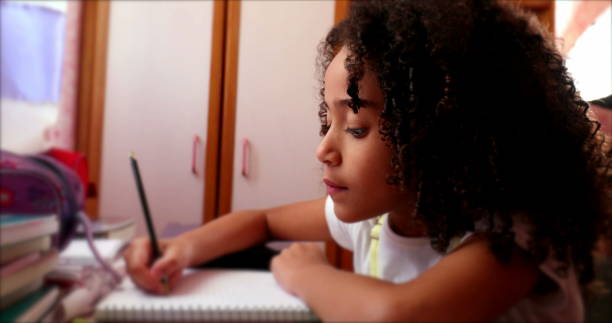 Ethnically diverse little girl child writing notes with pen. kid studying at home doing homework stock photo