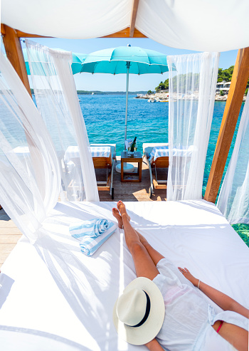 Woman resting on a luxurious day bed lounge at an exclusive luxury resort. The ocean can be seen in the background.