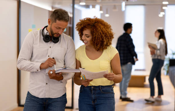 istock Young business colleagues at a startup company looking at some documents while standing in the corridor's office 1457193263