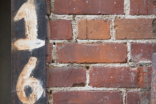 The number 16 sixteen is hand-painted on an old historic red brick wall in Redlands, California, USA.