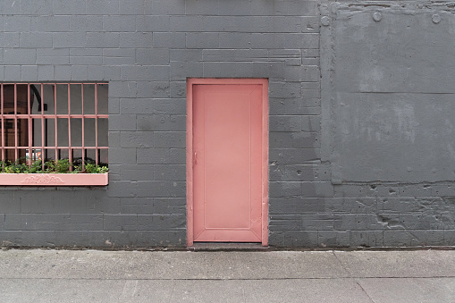 Minimal pink door of a restaurant with a gray brick wall alley and window in downtown Seattle, Washington, USA.