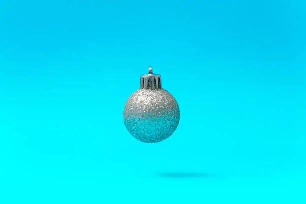 Silver Christmas Ball Ornament Floating in Mid-Air on a Turquoise Blue Background.