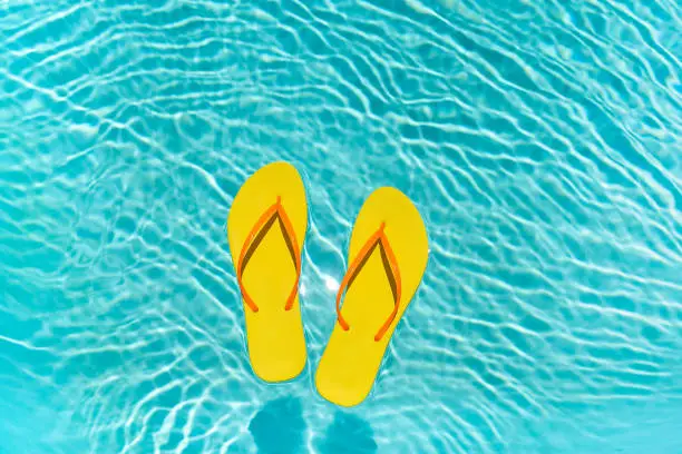 Yellow Flip Flops with orange straps floating in a clear blue swimming pool water on a bright sunny summer day.