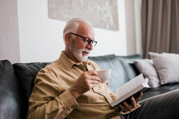 Senior man resting at home, drinking coffee and reading book