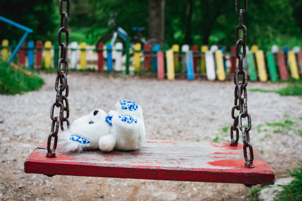 teddy bear lying on an empty swing in the park. sadness - swing playground empty abandoned imagens e fotografias de stock