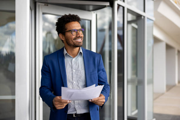 Business man leaving an office building holding documents and smiling