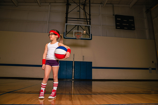 A young girl dressed in retro basketball attire with headband and wristbands gets ready for recreational league game. Image taken in Utah, USA.