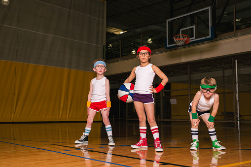 Two young boys and a girl are dressed in retro basketball attire with headbands and wristbands getting ready for recreational league game. Image taken in Utah, USA.