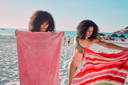 Woman, friends and beach towel for relaxing on the sand during summer break or vacation together in the outdoors. African American female women opening towels to relax on the sandy ocean coast