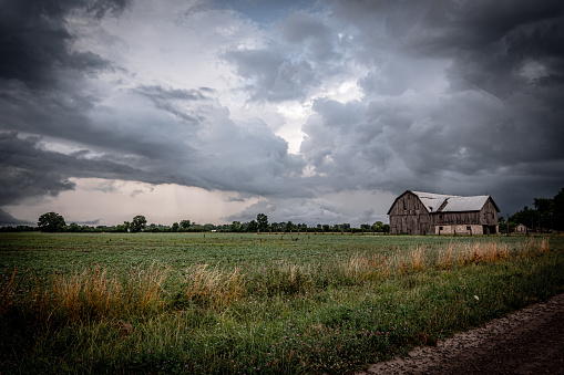 An old barn stands in a rural field under imposing, incoming storm clouds.