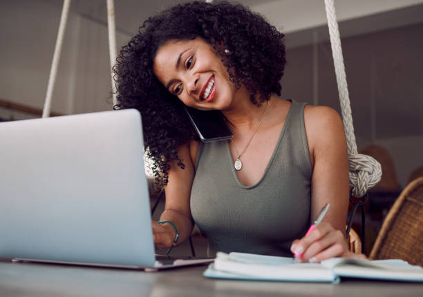 istock Black woman, phone call and laptop with smile for communication, networking or multitasking at home. African American female event planner smiling and writing in notebook for scheduling appointments 1457201569