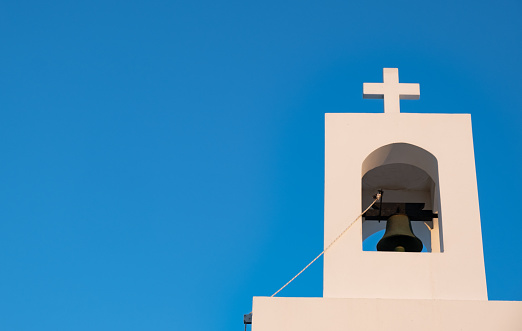 White christian belfry with orthodox cross on a greek church against blue sky. Faith and religion temple