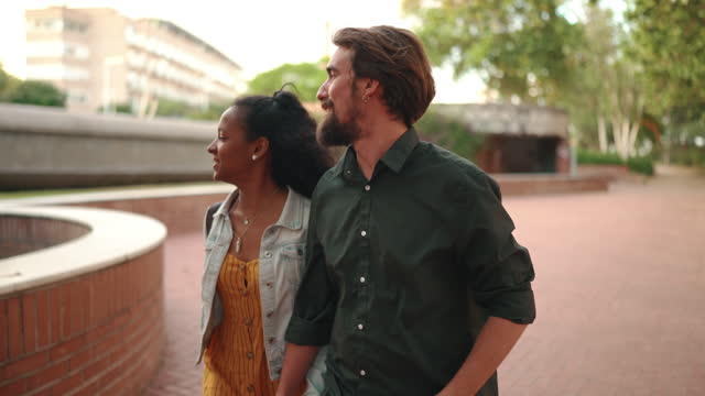 Closeup, man and woman walking smiling holding hands. Close-up of a young interracial couple in love going on a city street. Camera moves around the people