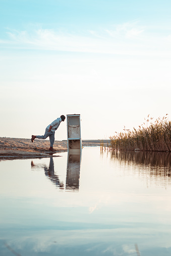 Photo of a boy looking at an abandoned fridge reflected in water