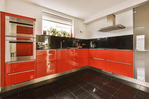 Fragment of interior of light narrow home kitchen with minimalist style red furniture with sink and stove