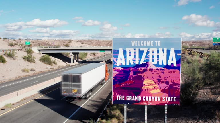 Trucks Driving by Arizona Border Sign