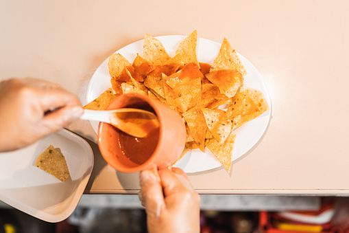High angle view of the hands of a cook dipping nachos in spicy sauce in a restaurant kitchen
