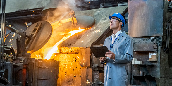 Waist up of man with hardhat standing in metallurgy plant  with digital tablet and checking production process.