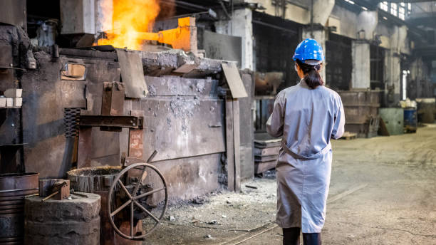 Back view of woman wearing work coat and hardhat. Female engineer standing in factory workshop and checking production process.