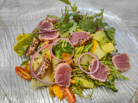Close-up shot of healthy salad with herb crusted tuna takaki, green leaf vegetable, cherry tomato slices, rucola and red onion.