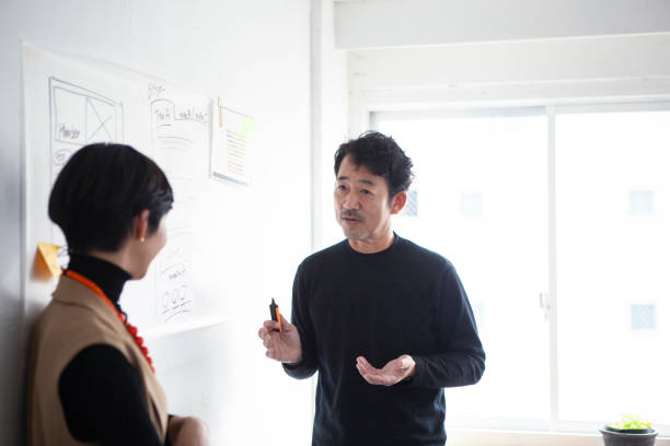 istock Middle-aged Asian engineer man in front of a whiteboard having an enthusiastic discussion with a team member 1457254130