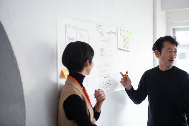 istock Middle-aged Asian engineer man in front of a whiteboard having an enthusiastic discussion with a team member 1457254137