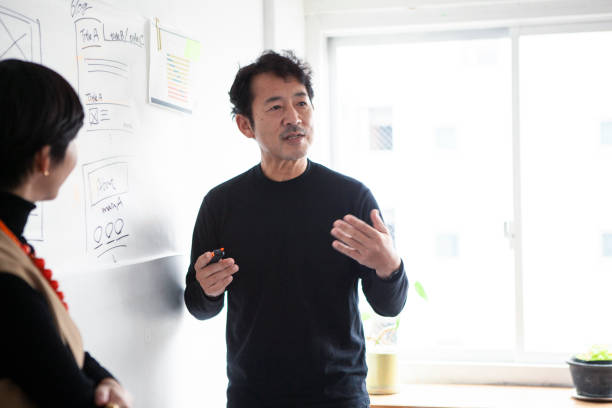 Middle-aged Asian engineer man in front of a whiteboard having an enthusiastic discussion with a team member