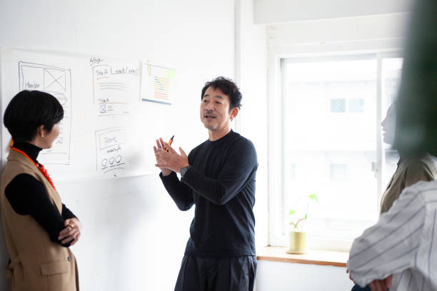 istock Middle-aged Asian engineer man in front of a whiteboard having an enthusiastic discussion with a team member 1457254142