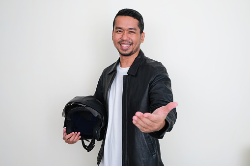 Adult Asian man wearing black leather jacket and holding motorcycle helmet offering help