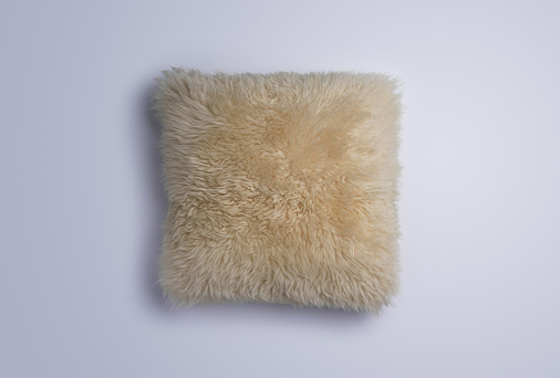 Overhead view of fluffy white sheepskin throw pillow on a white background