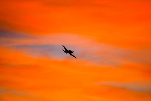Single-engine airplane landing against an orange sunrise backdrop.