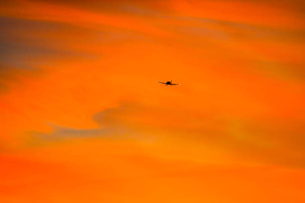 Single-engine airplane flying during a sunrise with orange clouds.