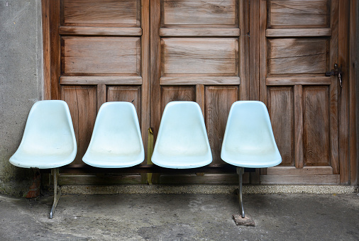 bench, a row of old light blue plastic chairs on cement floor with wooden door background, a lonely concept