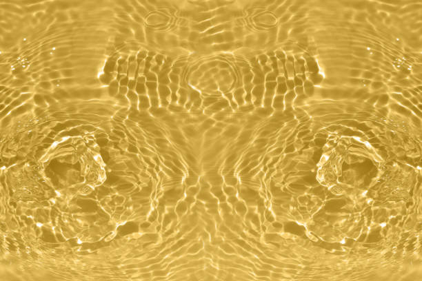 Defocus blurred transparent gold colored clear calm water surface texture with splashes and bubbles. Trendy abstract nature background. Water waves in sunlight with caustics. Yellow water shinning