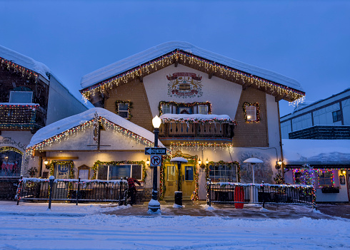 Street and buildings with Christmas lighting decoration in a snowy morning in Bavarian themed town of Leavenworth, Washington, USA. Man shoveling snow at the store front.