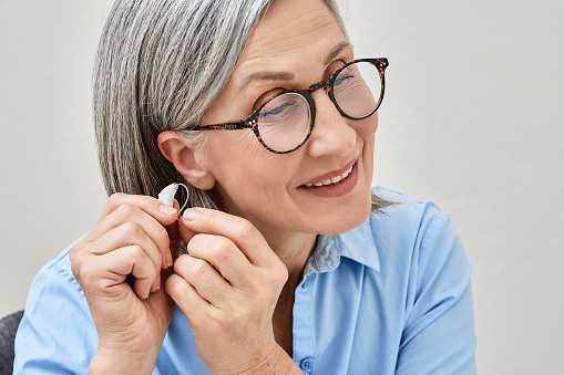 Grey-haired mature woman with hearing impairment using hearing aid. Hearing solutions for deafness people