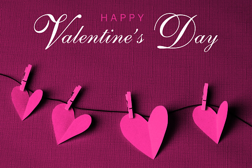 Pink paper cut hearts hanging on a clothesline with wooden clothespins. HAPPY VALENTINE'S DAY text is in the center. Can be used as a design for Valentine's day holiday greeting cards or posters.