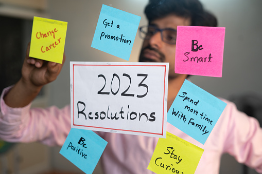 young man pasting 2023 Resolutions using sticky notes at office - concept of new year preparation and goal setting.