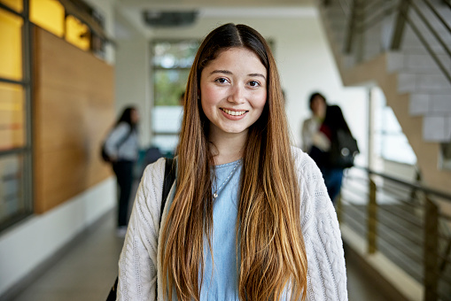 Waist-up view of longhaired woman in casual attire standing in hallway and smiling at camera. Property release attached.