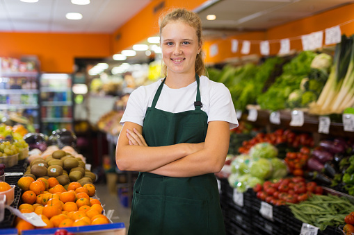 Friendly teenage girl vegetable shop seller posing in a work apron during her first day on a job