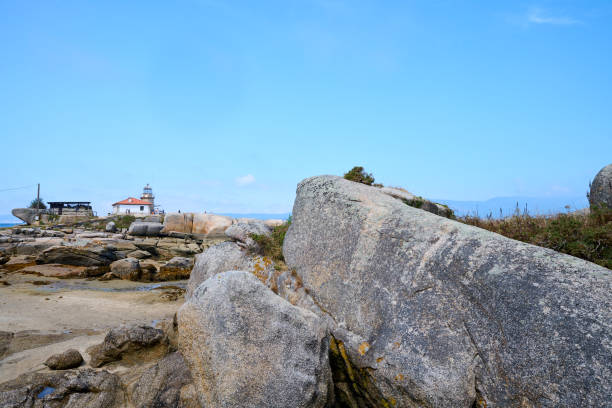 sandy beach with large rocks and a lighthouse on a sunny day