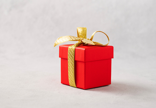 A red gift box with a gold ribbon on a gray background. The concept of holiday photography. Surprise for Valentine's Day, birthday, wedding. Copy space and front view.