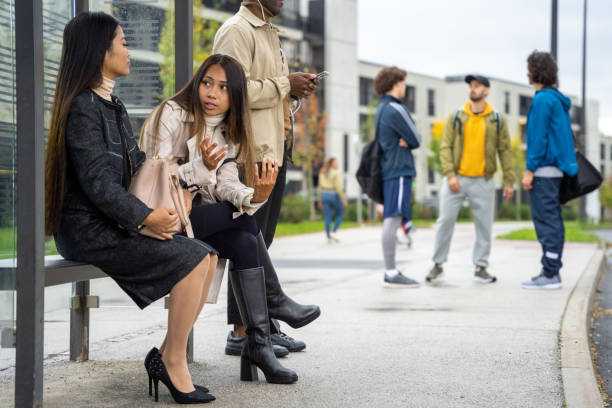 istock Two latin young women chatting at bus stop, side view 1457298183
