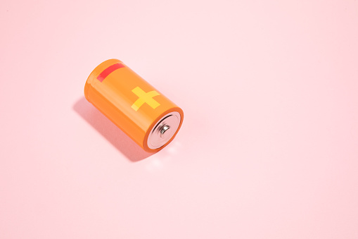 Orange battery on pink background, energy concept