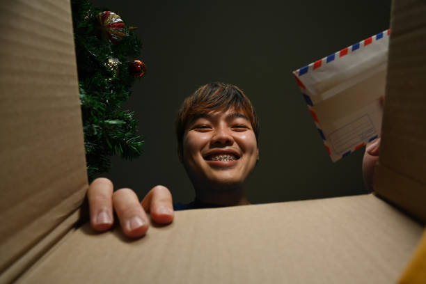 istock Smiling young asian man holding greeting card looking inside cardboard box. Shipping services, online shopping concept. 1457299823
