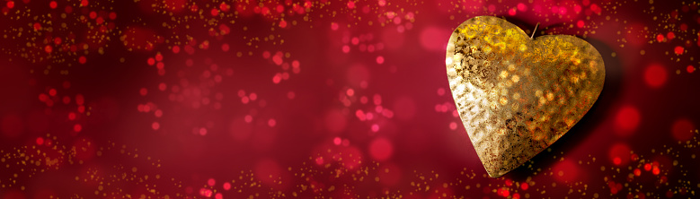 Heart of gold on a red background with bokeh bubbles and glitter in wide panoramic format, love symbol, valentines or mothers day concept, copy space, selected focus