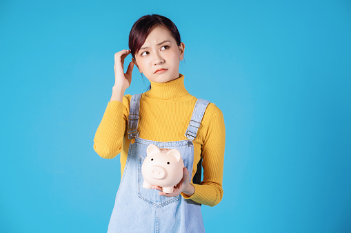 Young Asian girl holding piggy bank on blue background