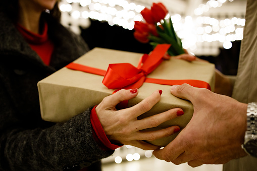 Man gives to his woman a gift box with red ribbon.