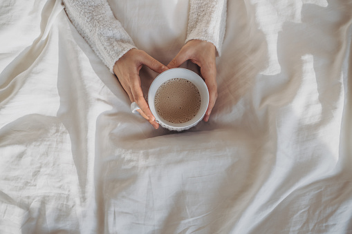 Close up of woman's hands holding coffee cup over blanket