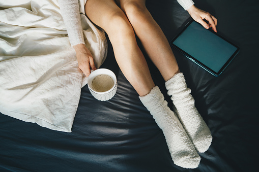 Woman relaxing in bed with a cup of coffee and digital tablet